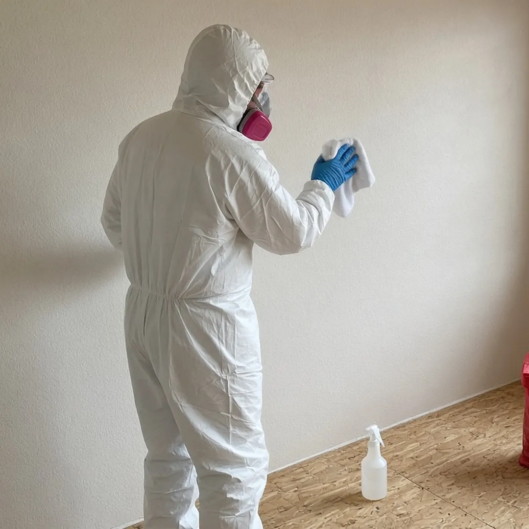 Technician in protective gear wiping down a bedroom wall during suicide cleanup in Arlington